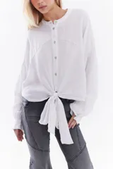 Camisa blanca de lino italiano, de corte holgado, mangas largas abullonadas, cuello mao y cierre frontal con botones, con diseño para anudar en la cintura.