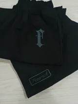 Bermuda de gabardina color beige con corte holgado. Presenta un bordado en tipografía gótica en la pierna derecha y un parche rectangular con el logo de la marca en la pierna izquierda. Cuenta con cintura elástica y bolsillos laterales.
