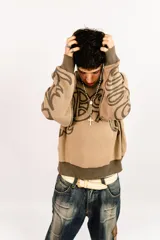 Sweater tejido reversible de corte boxy fit, con cuello redondo y puños acanalados. Presenta un diseño gráfico abstracto de estilo gótico que recorre el pecho y las mangas. Un lado es de color marrón oscuro con detalles en beige, y el otro lado es de color beige con detalles en marrón oscuro.