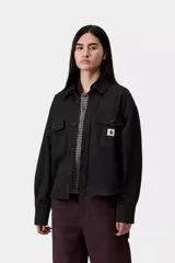 Chaqueta tipo camisa Carhartt WIP modelo Kelly, de color negro, confeccionada en sarga de algodón sin forro. Presenta cierre frontal de botones, bolsillos delanteros en el pecho con solapa, cuello camisero, hombros caídos y una etiqueta cuadrada tejida de la marca.