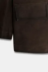 Blazer de mujer color marrón oscuro, confeccionado en piel de ante 100%. Presenta cuello solapa de muescas, manga larga, bolsillos de plastrón frontales y cierre frontal de botones.