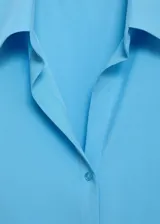 Camisa de corte recto y tejido fluido, con cuello camisero, cierre frontal de botones y mangas largas con puños abotonados.