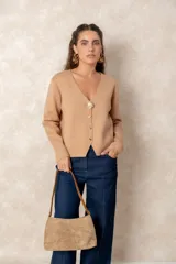 Cartera de hombro confeccionada en gamuza color beige, con detalles en cuero sintético marrón en las manijas y bordes. Presenta un diseño minimalista y funcional con cierre superior.