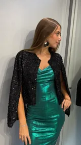 Chaqueta corta de color negro, confeccionada en tejido cubierto de lentejuelas brillantes. Presenta un diseño abierto sin cierre frontal, con mangas tipo capa que aportan un estilo elegante y sofisticado.
