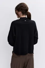 Sweater de punto negro con cuello alto y detalle de ojalillos metálicos a lo largo de las mangas. Presenta un corte holgado con puños y ruedo acanalados.