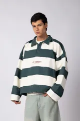 Buzo tipo polo de corte boxy, con diseño de franjas horizontales anchas en color verde oscuro y crema. Presenta cuello camisero, cierre frontal parcial y detalles de costuras desflecadas. Incluye logo bordado en el pecho.