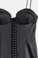 Vestido corto satinado negro con escote corazón, tirantes finos y cierre frontal con corchetes metálicos.