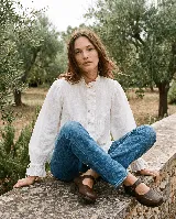Camisa romántica blanca de algodón, de silueta holgada y manga larga. Presenta detalles de tablas y volados en el frente, cuello alto con volado y puños ajustables.