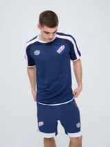 Remera deportiva de entrenamiento Umbro del Club Nacional de Football, color azul marino con detalles en blanco y líneas rojas en los hombros. Cuenta con el logo de la marca y el escudo del club en el pecho.