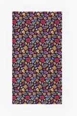 Pareo de algodón con estampado vibrante sobre fondo negro. El diseño presenta figuras abstractas y estilizadas en tonos de azul, rojo, amarillo y morado, con un borde deshilachado.