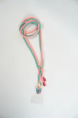 Correa para celular de diseño trenzado, confeccionada con cordones en colores turquesa y naranja. Incluye herrajes metálicos y terminales de goma en color fucsia, con un adaptador transparente para sujetar el dispositivo.