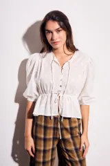 Blusa negra de algodón con diseño de broderie, mangas tres cuartos abullonadas, cierre frontal con botones y detalle de cordón ajustable en la cintura.