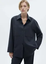 Camisa de corte recto con diseño de raya diplomática, cuello camisero, cierre frontal de botones y dos bolsillos de parche delanteros. Presenta mangas largas con puños rectos.