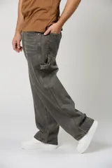 Pantalón de jean estilo baggy con corte holgado y diseño de carpintero, en color gris oscuro con efecto lavado. Presenta costuras reforzadas en contraste y bolsillos laterales funcionales.