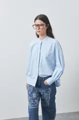 Camisa de manga larga en color celeste, con cuello mao y cierre frontal oculto. Presenta un diseño de silueta relajada con sisa caída y un bolsillo aplicado en el pecho.