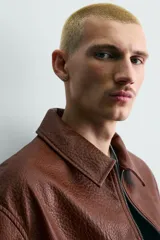 Sobrecamisa de corte relajado confeccionada en tejido efecto piel, con cuello solapa, manga corta, bolsillo plastrón en el pecho y cierre frontal con cremallera.