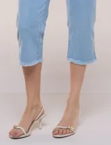 Capri blanco de corte ajustado, con tiro alto y pretina ancha elastizada tipo faja. Presenta bolsillos falsos al frente con remaches, piernas entalladas con pequeñas aberturas en los laterales y ruedo desflecado.