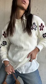 Sweater de punto color natural con cuello redondo y diseño de flores bordadas en las mangas. Presenta puños y ruedo acanalados.