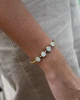 Pulsera rígida dorada con cuatro piedras redondas de nácar engarzadas.
