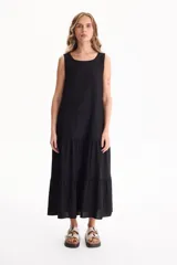 Vestido largo negro de lino, sin mangas, con escote redondo y diseño fluido con volados escalonados en la falda.