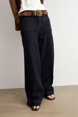 Pantalón de jean azul oscuro con corte flare, tiro alto y bolsillos delanteros tipo plaqué. Presenta costuras a la vista y una silueta amplia en las piernas.