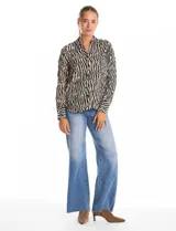 Camisa de manga larga con cuello solapa y cierre frontal de botones. Presenta un diseño estampado con patrón de cebra en tonos blanco y negro, puños abotonados y ruedo redondeado.