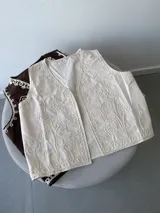 Chaleco marrón con bordados florales en color crema en los bordes y el frente. Presenta un diseño sin mangas con escote en V.