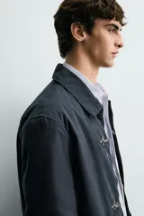 Parka de corte relajado confeccionada en mezcla de algodón color marrón. Presenta cuello solapa, cierre frontal con cremallera oculta y alamares metálicos, bolsillos de plastrón con solapa en la cadera y bolsillo de vivo en el pecho.