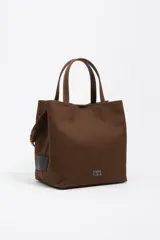 Bolso tipo tote de Bimba y Lola en color marrón, confeccionado en gabardina con detalles en piel. Cuenta con doble asa de mano, asa bandolera regulable, cierre con botón de presión y logo metálico aplicado en el frente.