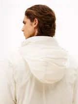 Campera ligera color crema, con cuello alto y cierre frontal de cremallera. Presenta un pequeño logo bordado de Tommy Hilfiger en el pecho.