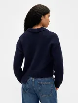 Buzo tipo polo de tejido de punto, color azul marino, con cuello solapa, escote en V y logo de la marca bordado en el pecho. Presenta mangas largas y un diseño de ruedo asimétrico con detalle acanalado.