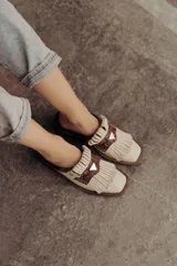 Zueco de cuero color crudo, con diseño destalonado, punta cuadrada, detalle de flecos y una pieza central de cuero con estampado snake en tonos marrones y un aplique metálico triangular.