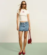 Pollera mini de jean color negro, con cintura mediana, trabillas para cinturón, bolsillos laterales y cierre frontal con botón y cremallera.