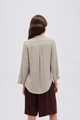 Blusa de viscosa color beige con cuello en V, cierre parcial de botones frontales, bolsillo en el pecho y mangas 3/4.