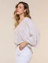 Blusa de algodón y rayón color beige, de la marca Dash. Presenta diseño texturado con sutiles rayas verticales, escote en V cruzado, mangas tres cuartos amplias y ruedo elastizado.