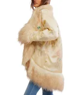 Chaqueta estilo kimono o bata, color crema o amarillo pálido, con acabado satinado y bordados florales sutiles. Presenta un ribete y puños voluminosos de pelo sintético largo y rizado en tono beige/crema.