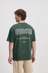 Remera oversize verde oscuro de manga corta, con estampa geométrica y texto en la espalda.