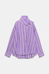 Camisa de corte oversize con diseño de rayas verticales en tonos violeta, blanco y bordó. Presenta cuello subido cruzado con cierre de botones frontal, mangas largas con puños y bajo asimétrico.