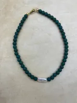 Collar artesanal compuesto por cuentas de piedra volcánica en diversos tonos y tamaños, con una perla natural de río como dije central y cierre metálico dorado.