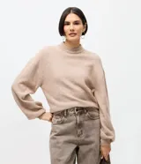 Suéter corto de punto en color beige, con cuello alto y mangas largas con puños ajustados. Presenta un diseño de calce holgado y tejido de textura suave.