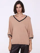 Sweater color beige de tejido de punto, con escote en V con borde negro y mangas 3/4 con puños con detalle de botón dorado.