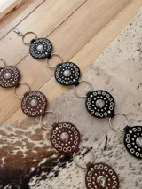 Cinturón de cuerina compuesto por piezas circulares unidas mediante argollas metálicas. Cada pieza de cuerina presenta tachas y un aplique metálico central con diseño grabado.