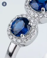 Anillo de plata 925 con diseño de tres piedras, presentando una circonia azul central de corte ovalado rodeada por un halo de pequeñas circonias blancas, flanqueada por dos circonias azules laterales más pequeñas.