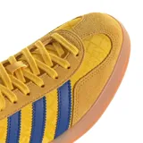 Championes Adidas Gazelle Indoor con exterior de gamuza amarilla y estampado geométrico sutil. Presenta las tres tiras laterales en azul, detalle en el talón en color rojo y suela de caucho color caramelo.