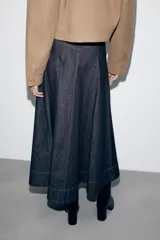 Falda midi de denim en color azul oscuro, con diseño evasé, bolsillos delanteros, costuras pespuntadas en contraste y cierre frontal con cremallera y botón metálico.