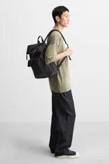 Mochila verde militar con acabado engomado, solapa superior con cierre de hebilla y cremallera, bolsillo frontal con cierre imantado, compartimento interno para laptop de hasta 13 pulgadas, asa de mano superior, correas de hombro ajustables y espalda acolchada. Base de cuero sintético negro.