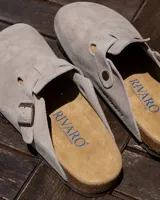 Zuecos de cuero gamuzado color gris con diseño de punta cerrada y correa ajustable con hebilla metálica. Poseen plantilla anatómica de corcho y suela de goma.