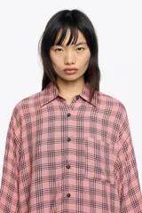 Camisa de manga 3/4 con cuello camisero, silueta ancha y bolsillo de plastrón en el pecho. Presenta un estampado de cuadros en tonos rosado y negro.