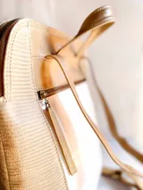 Mochila de diseño tricolor con paneles en beige, blanco con textura tipo reptil y detalles en cuero sintético marrón. Cuenta con un bolsillo frontal con cierre, correas ajustables y etiqueta de marca en la parte inferior.