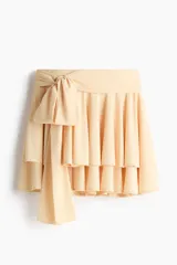Pollera mini escalonada de punto de crepé color beige, con pretina ancha y cinturón para atar lateralmente en forma de lazo.